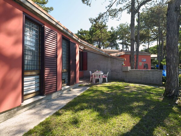 Un bâtiment à la façade rouge, un petit patio avec une table et des chaises, et un espace verdoyant.