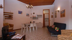 A cozy living room with a dining area, a kitchen in the background, and a TV on the left. - Beautiful apartment for 7 people with A/C, TV, terrace and pets allowed (Lignano Sabbiadoro)