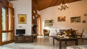 A cozy living room with a fireplace, a television, wicker chairs, a dining table, and patterned floor tiles. - Beautiful apartment for 7 people with A/C, TV, terrace and pets allowed (Lignano Sabbiadoro)