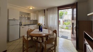 A compact kitchen with white cabinets, a refrigerator, and a dining table with chairs. - Beautiful apartment for 5 people with A/C, WIFI, TV, patio and pets allowed (Lignano Sabbiadoro)