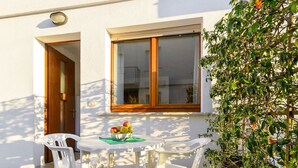 A white outdoor seating area with a table and two chairs, a bowl of fruit on the table, and a potted plant to the right. - Beautiful apartment for 5 people with A/C, WIFI, TV, patio and pets allowed (Lignano Sabbiadoro)