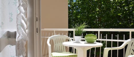 A balcony with white chairs and a table, a potted plant, and a green bowl.