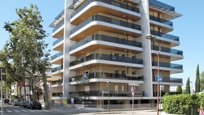 A multi-story building with balconies, a clear sky, and a street with cars and trees. - Cosy apartment for 6 guests with WIFI, A/C, TV and balcony (Lignano Sabbiadoro)