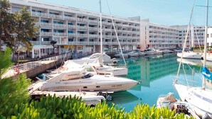 Een jachthaven met verschillende jachten in de haven, een groot hotelgebouw met balkons, en weelderige begroeiing op de voorgrond.