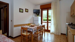 A compact kitchen with a dining area, a TV mounted on the wall, and a sliding glass door leading to a garden. - Lovely apartment for 5 guests with A/C, pool, TV, patio and pets allowed (Lignano Sabbiadoro)