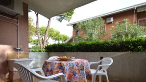 A patio with a table covered by a colorful tablecloth, two white plastic chairs, and a bowl of fruit. - Lovely apartment for 5 guests with A/C, pool, TV, patio and pets allowed (Lignano Sabbiadoro)