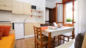 A compact kitchen with wooden cabinets, a microwave, and a sink. There is a dining area with a table, chairs, and a laptop. - Lovely apartment for 5 guests with A/C, pool, TV, patio and pets allowed (Lignano Sabbiadoro)