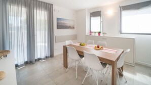 Ein zeitgemäßer Essbereich mit einem Holztisch, weißen Stühlen und Blick ins Freie durch große Fenster.