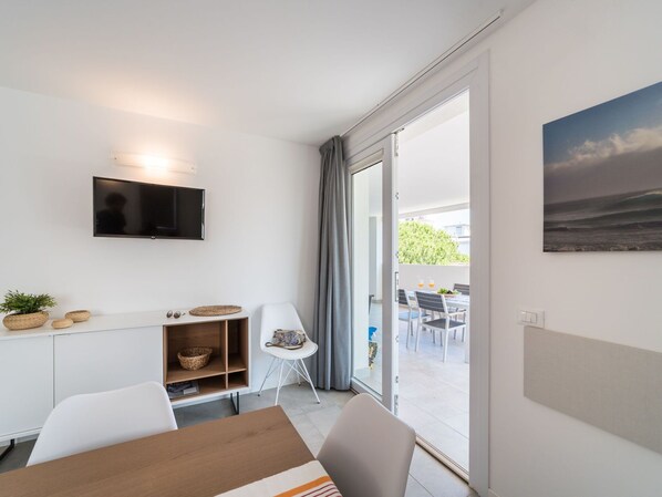 Une chambre moderne dotée d’un téléviseur à écran plat fixé au mur, d’une table à manger avec des chaises, d’un petit meuble blanc et offrant une vue sur l’extérieur grâce à une porte-fenêtre coulissante.
