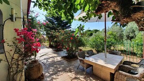 Un patio al aire libre con una mesa y sillas, rodeado de macetas con plantas y arbustos florecientes.