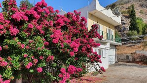 Un edificio con un balcón y un gran arbusto de flores rosadas al frente.