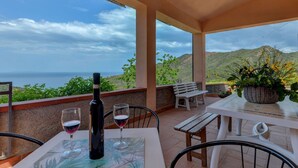 A terrace with a table set for two, a bottle of wine, and a glass of wine. The terrace overlooks a scenic view of the sea and hills. - Beautiful apartment for 4 people with WIFI, TV, terrace and pets allowed (Rio Nell'elba)