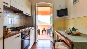 A compact kitchen with a stove, oven, and sink, leading to a balcony with a table and chairs. - Beautiful apartment for 4 people with WIFI, TV, terrace and pets allowed (Rio Nell'elba)