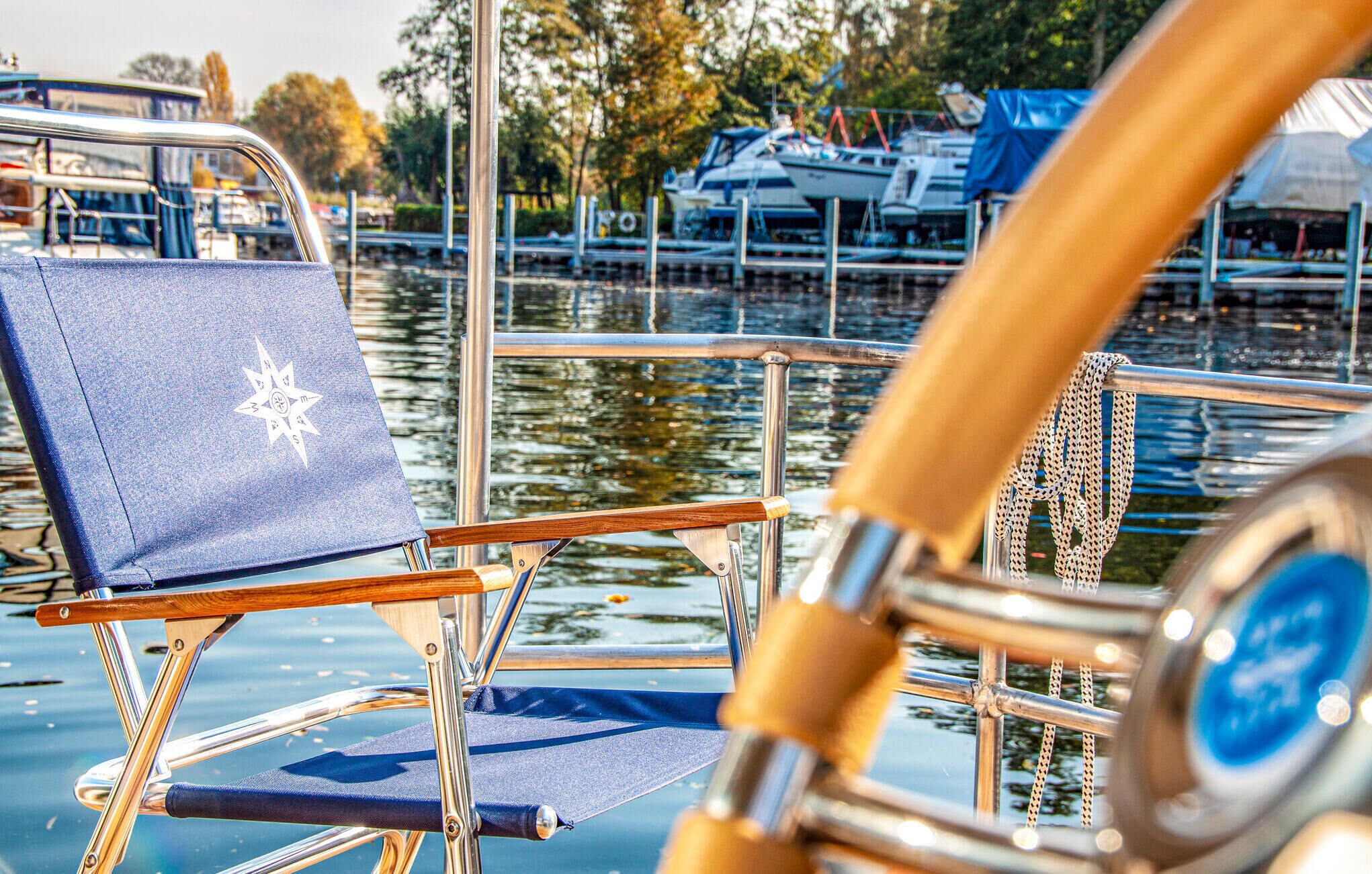 A boat's deck with a blue chair and a steering wheel.