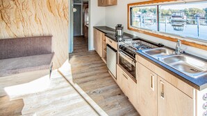 A modern kitchen with wooden cabinets, a stainless steel sink, and a window overlooking a water body. - Awesome ship in Hennigsdorf with lake view (Hennigsdorf)