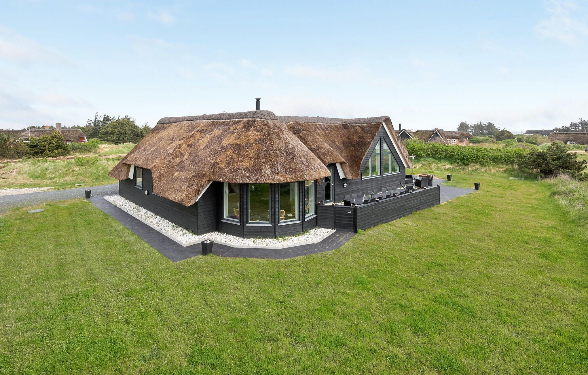 Une maison moderne avec un toit de chaume, de grandes fenêtres et un patio.