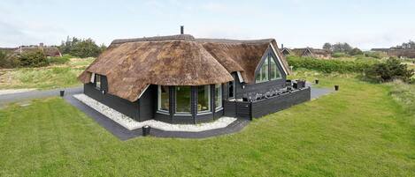 Une maison moderne avec un toit de chaume, de grandes fenêtres et un patio.