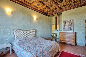 Ein Schlafzimmer mit einer geblümten Bettdecke, einem gepolsterten Kopfteil, einer Holzkommode und einem Bild an der Wand.