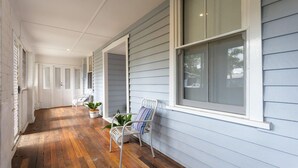 A covered porch with wooden flooring, white metal chairs, and potted plants.
