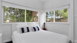 A bedroom with a large bed, two windows, and a guitar against the wall.