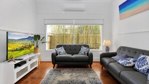 A living room with a sofa, a television, and a large window with a view of bamboo.