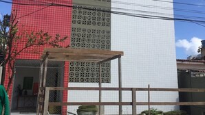 Un bâtiment à la façade rouge et blanche, un espace extérieur couvert doté d’une structure en bois, et une brouette remplie de plantes.