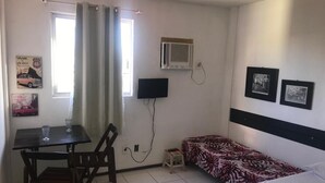 Une chambre avec un lit, un bureau et une chaise, une télévision et une fenêtre avec des rideaux.