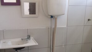 Une petite salle de bain avec un lavabo blanc, des toilettes et un réservoir de chasse d’eau fixé au mur.