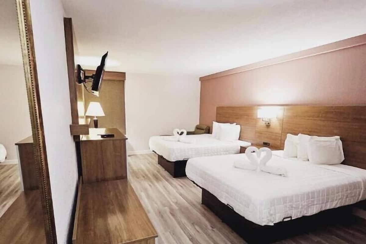 Quarto de hotel com duas camas, uma escrivaninha, um espelho e uma televisão.