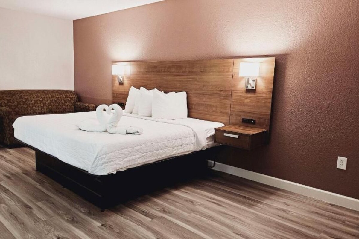 A hotel room with a wooden bed, a nightstand, a small table, and a brown upholstered bench.