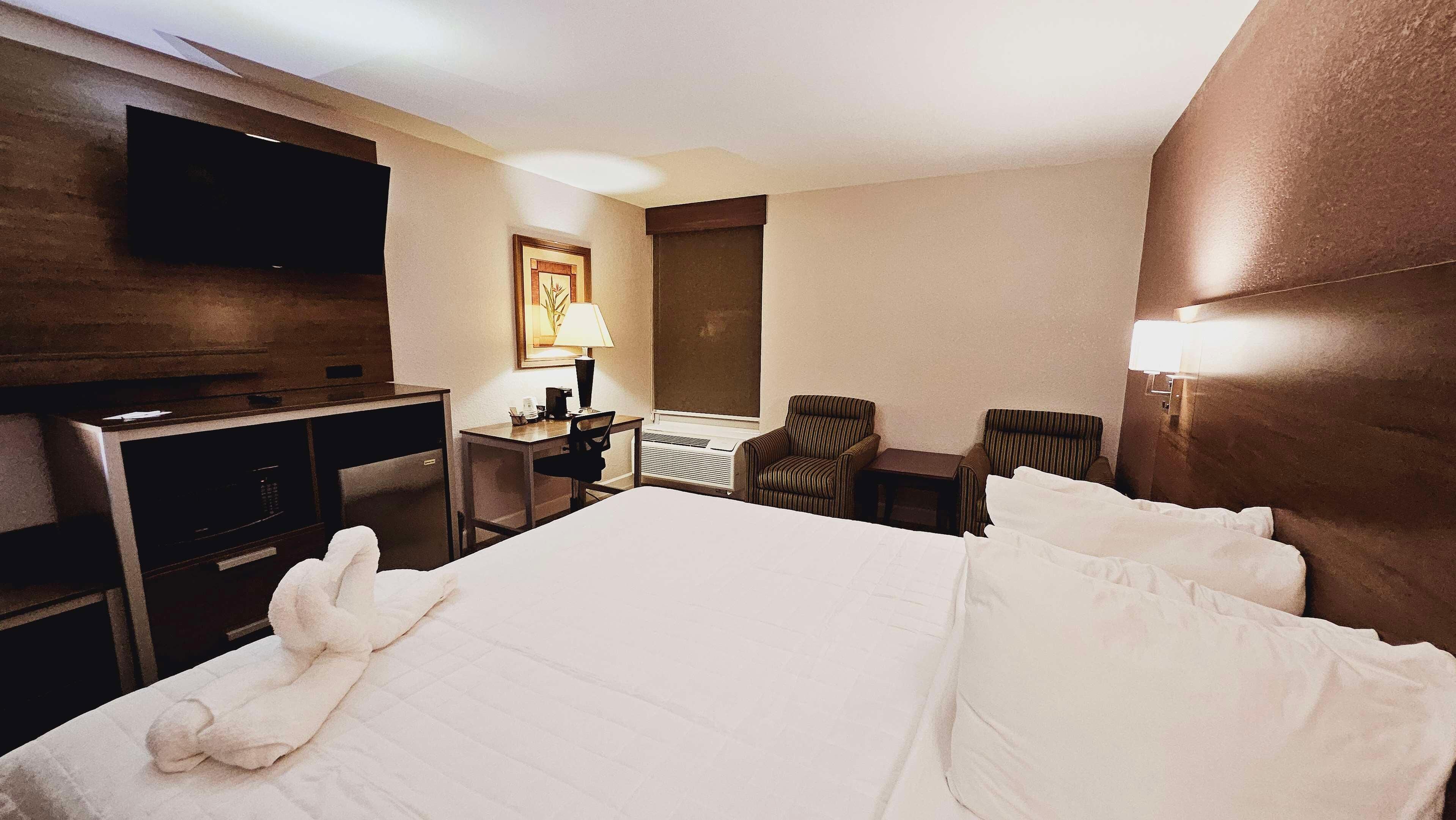 Habitació d'hotel amb llit, escriptori, cadira, televisió i finestra.