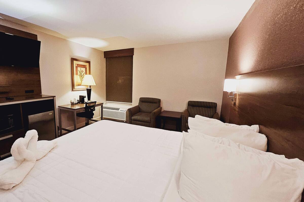 Quarto de hotel com cama, escrivaninha, cadeira, televisão e janela.