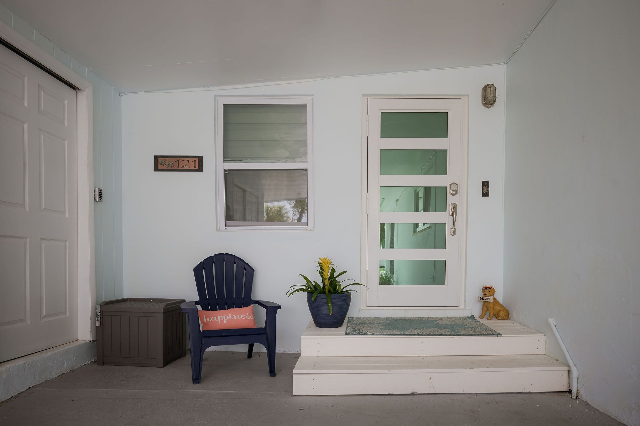 A front porch with a bench, a potted plant, and a welcome sign.