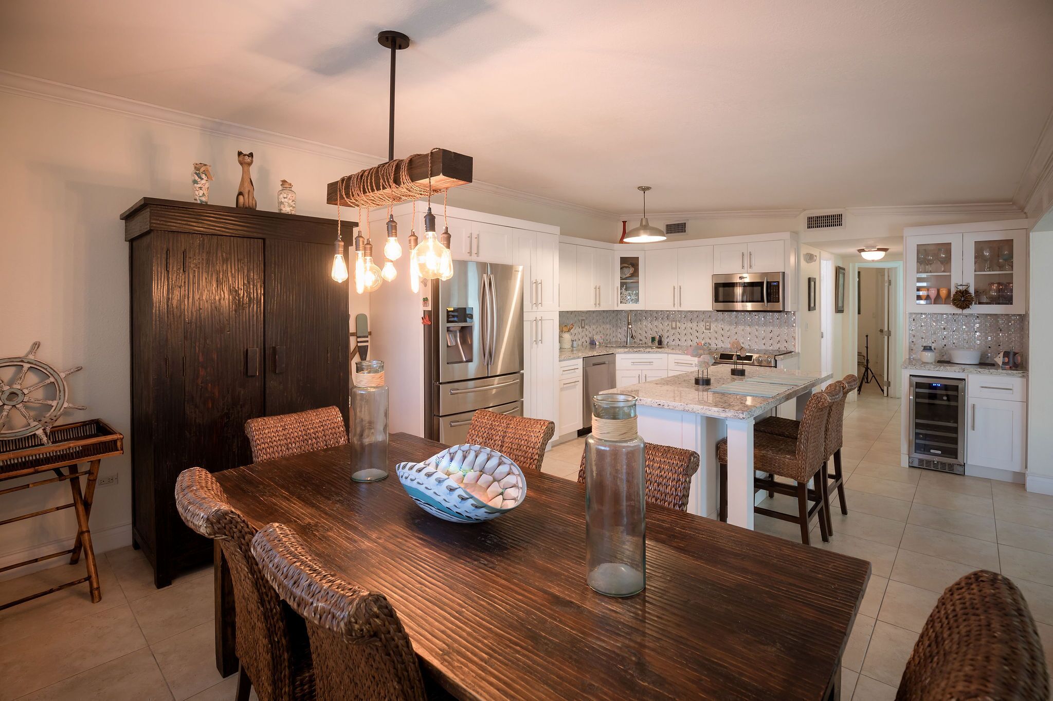A modern kitchen with white cabinetry, stainless steel appliances, and a wooden dining table with wicker chairs.
