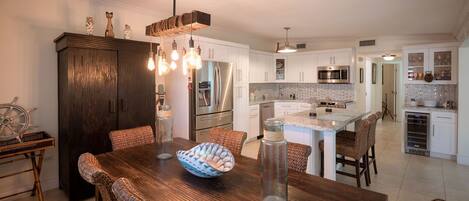 A modern kitchen with white cabinetry, stainless steel appliances, and a wooden dining table with wicker chairs.