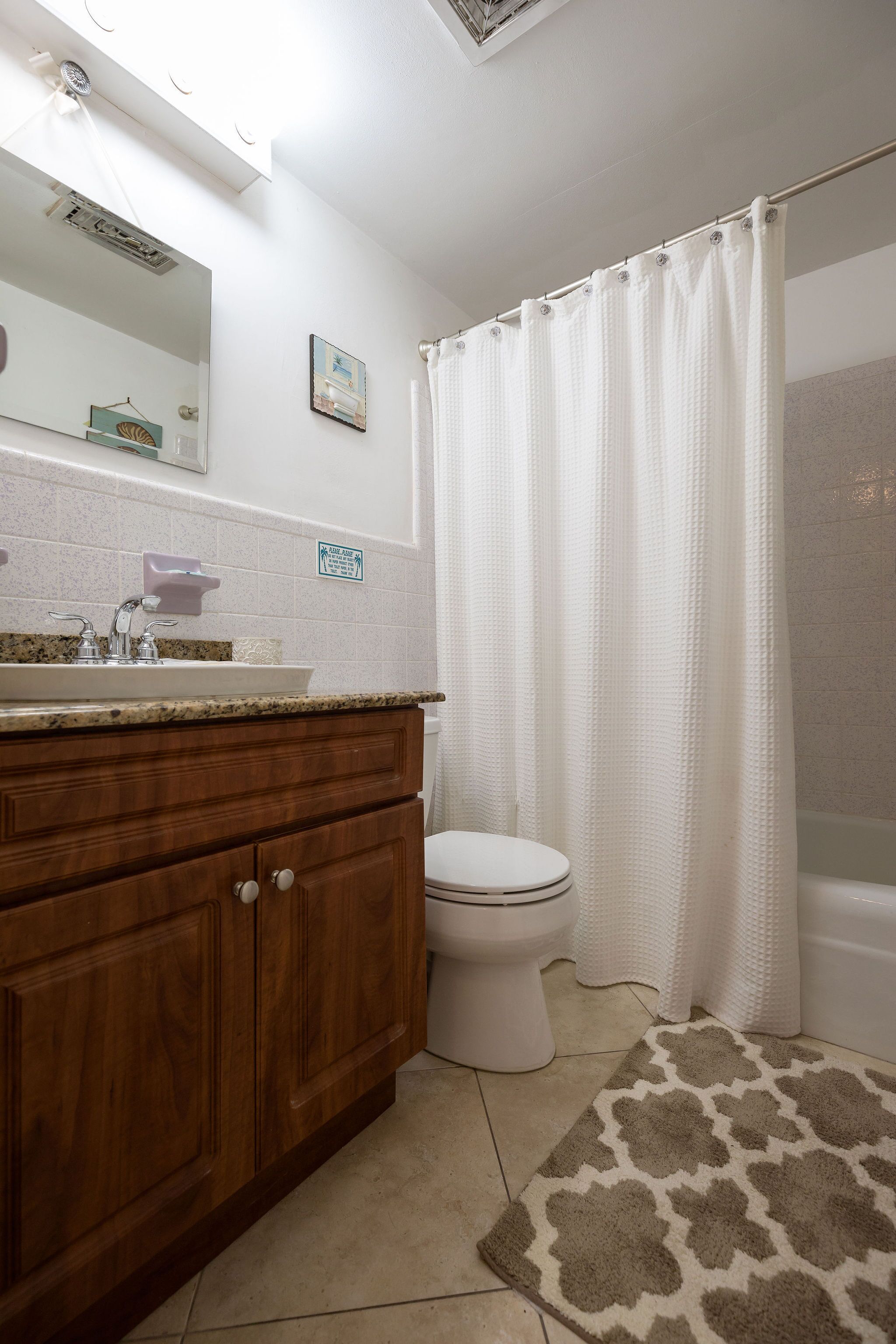 A bathroom with a wooden vanity, a toilet, a shower curtain, and a patterned rug.