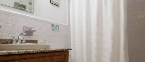 A bathroom with a wooden vanity, a toilet, a shower curtain, and a patterned rug.