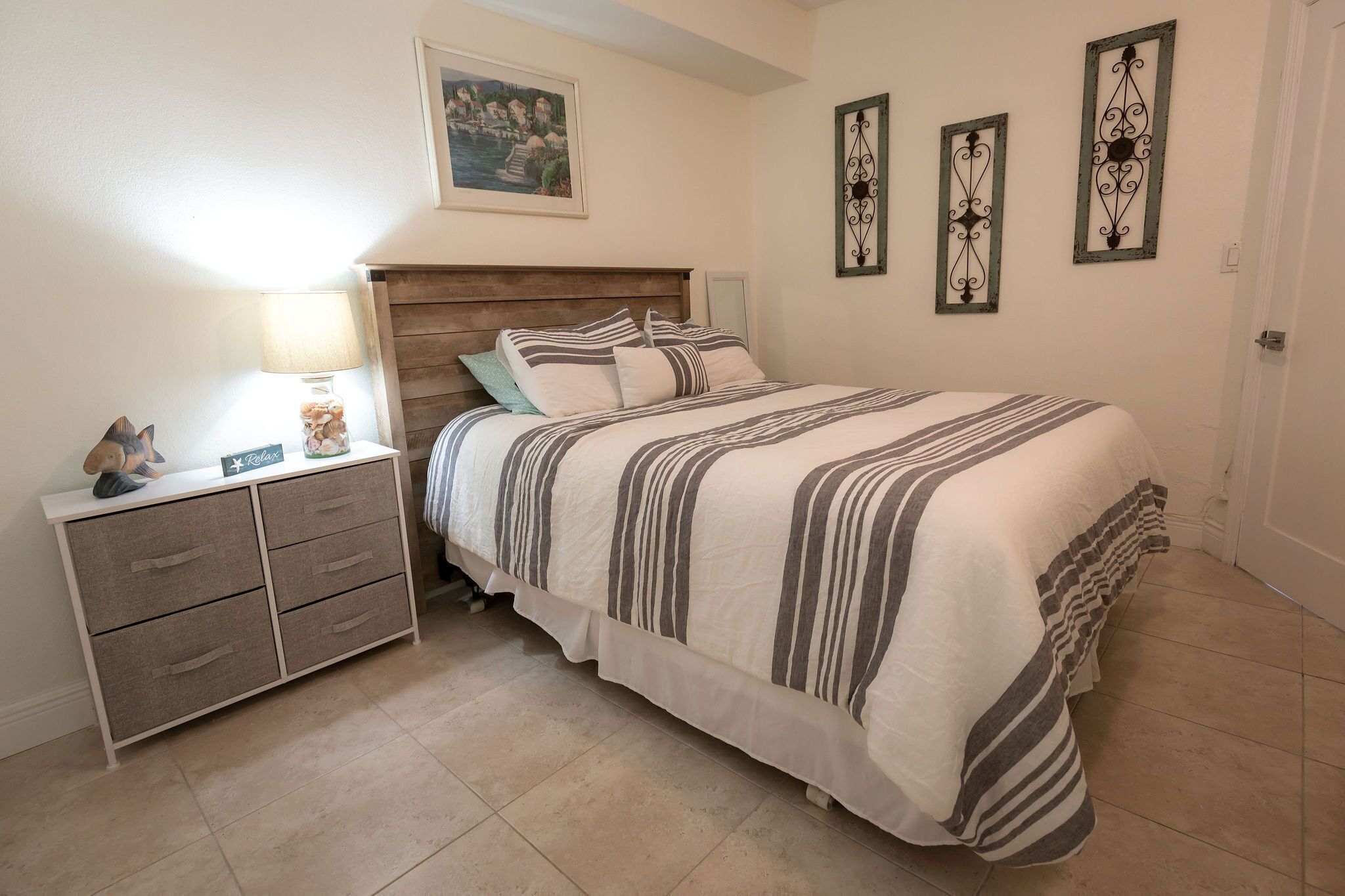 A bedroom with a bed, bedside table, lamp, and a dresser.