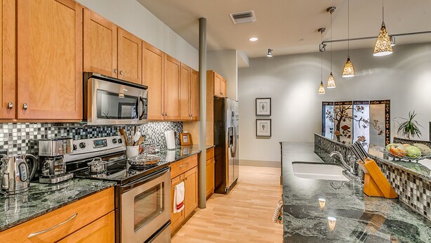 A modern kitchen with wooden cabinets, stainless steel appliances, and a marble countertop.