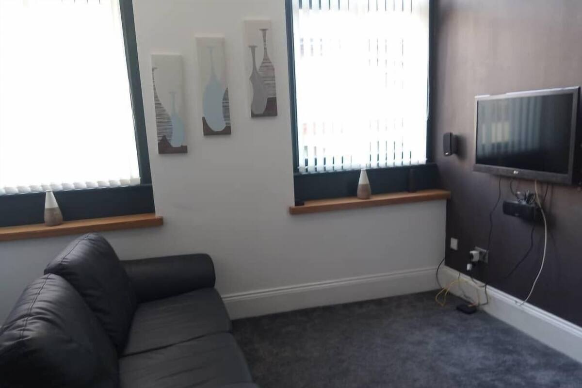 A living room with a black leather sofa, a flat-screen TV mounted on the wall, and three wall-mounted decorative vases.