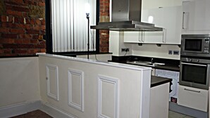 A modern kitchen with white cabinetry, a stainless steel range hood, and a built-in oven. - Premier Apartments (Bradford)