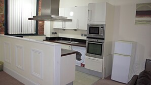 A compact kitchen with a washing machine, microwave, oven, and refrigerator. - Premier Apartments (Bradford)