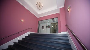 A staircase with a handrail, pink walls, and a chandelier. - Premier Apartments (Bradford)