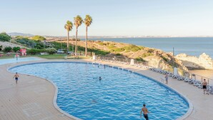 Una amplia piscina exterior de diseño curvo, rodeada por una solana empavedada y sillas de descanso.
