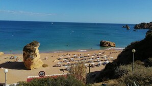 Una playa con agua azul cristalina, formaciones rocosas y un letrero que indica que no se permiten perros.