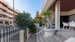Un balcón con piso de madera, una silla blanca para exteriores, una silla colgante y una planta en maceta.