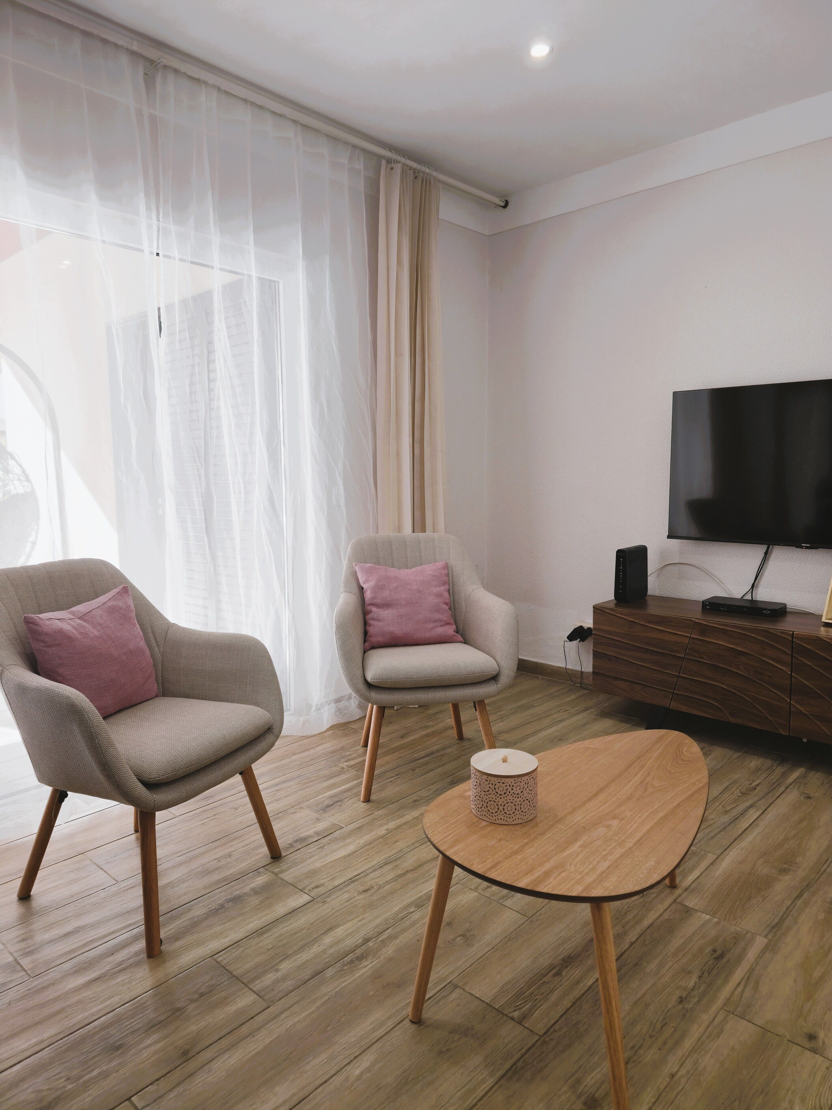 A modern living room with two armchairs, a coffee table, a television, and a wooden floor.