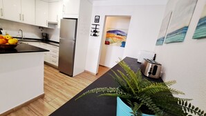 Een moderne keuken met witte kasten, een roestvrijstalen koelkast, een zwart aanrecht en een blauwe plant.