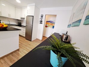 Cozinha moderna com armários brancos, geladeira de aço inoxidável, bancada preta e uma planta azul.