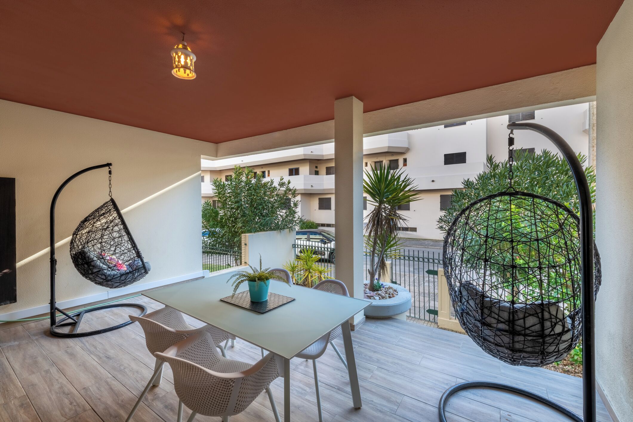 Een balkon met een tafel, stoelen, hangstoelen en potplanten.
